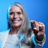 Senior woman with white hair showing small hearing aid Pure-Charge-and-Go 3AX 7AXi