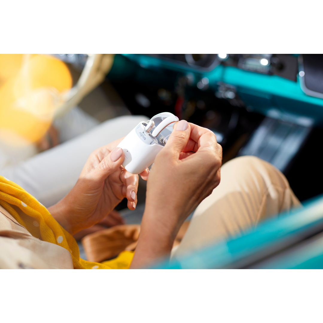 A woman sitting in a car is charging her Signia Styletto 3X/7X hearing aids with the white pocket-sized portable/nomad charging case 