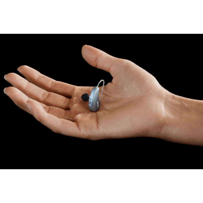 A woman holding the small Widex Moment hearing aid in the color grey in her hand